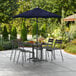 A Lancaster Table & Seating navy blue umbrella on a patio table with chairs.