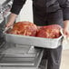 A woman using a Choice aluminum roaster pan to cook meat.