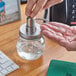 A hand using an American Metalcraft stainless steel mason jar lid with a pump to dispense hand sanitizer.