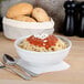 A Tuxton porcelain white bowl filled with spaghetti, sauce, and cheese on a table with a spoon and bread bag.