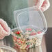 A gloved hand holding a Choice clear plastic deli container filled with food.