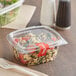 A clear Choice plastic deli container filled with salad with a plastic fork next to it.