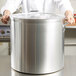A chef using a Vollrath Wear-Ever domed aluminum pot cover to hold a large silver pot.