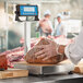 A person in a plastic glove weighing meat on an AvaWeigh receiving scale on a butcher shop counter.