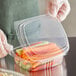 A gloved hand holding a Choice clear plastic deli container with vegetables.