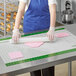 A person wearing gloves rolls out white dough on a green and white grid work mat.