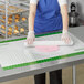 A person using a Baker's Mark green grid silicone work mat to roll out dough on a table.