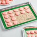 A Baker's Mark green silicone baking mat with pink macarons.