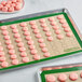 A Baker's Mark full size green silicone baking mat with pink macarons on it.