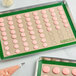 A Baker's Mark green silicone baking mat with pink macarons on it.