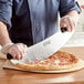 A person using a Choice 20" Rocking Pizza Cutter to cut a pizza.