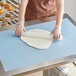 A woman using a Baker's Mark blue silicone work mat to roll out dough on a table.