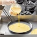 A person using a Vigor egg ring to pour yellow liquid into a pan.