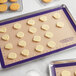 A Baker's Mark purple silicone baking mat with cookies on a tray.