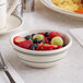 A bowl of fruit in a white Acopa stoneware bowl on a table with a fork and spoon.