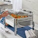 A person using a silver Acopa Manchester chafer stand to serve food.
