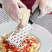 A hand grates cheese on a plate of pasta using a Choice stainless steel grater with a black handle.