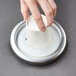 A hand putting a white cup into a metal tray with Carlisle medium cup dispenser gaskets.