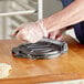 A person cutting a tortilla on a cutting board with a Choice cast iron tortilla press.