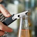 A person using the Choice All-in-One Waiter Corkscrew and Bottle Opener to open a bottle of champagne on a counter.