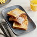 A rectangular melamine platter with a stack of french toast with powdered sugar on it on a table with a fork and knife.