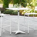 A white Lancaster Table & Seating bar height table with chairs and an umbrella on a patio.