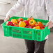 A person holding a green Choice Green Vented Agricultural Crate full of yellow and red bell peppers.