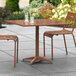 A Lancaster Table & Seating brown powder-coated aluminum outdoor dining table with two chairs on a patio.