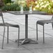 A Lancaster Table & Seating gray powder-coated aluminum outdoor table with two chairs on a patio.