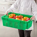 A person holding a Choice green vented agricultural crate full of yellow and red bell peppers.