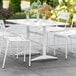 A white Lancaster Table & Seating outdoor dining table with chairs on a patio.