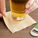 A hand holding a beer bottle and a beer glass over a table with EcoChoice natural kraft beverage napkins.