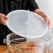 A person holding a Cambro translucent round food storage container with a lid over brown food.