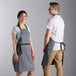 A man and woman wearing gray Choice bib aprons with black webbing accents.