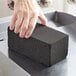 A hand using a Carlisle black brick to clean a metal surface.
