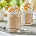 A glass mug of Capora Caramel Latte Frappe mix with whipped cream and caramel sauce on top.
