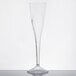 A clear WNA Comet plastic champagne glass with a curved stem on a white table.
