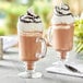 Two glasses of mocha frappe with whipped cream and chocolate drizzle on a table.