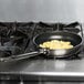A Vollrath Centurion stainless steel non-stick fry pan with scrambled eggs cooking on a stove.