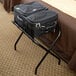 A black suitcase on a black Lancaster Table & Seating folding luggage rack.