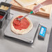 An AvaWeigh pizza scale being used to measure a pizza on a counter in a pizza parlor.