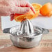 A hand squeezing an orange into a stainless steel citrus juicer on a counter.