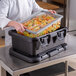 A chef using a Cambro food pan carrier to hold food.