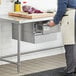 A person wearing an apron opens a Regency stainless steel drawer in a kitchen.