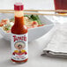 A bottle of Tapatio hot sauce next to a bowl of shrimp.