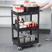 A person holding a black Luxor 3 tub utility cart.
