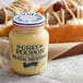 A jar of Grey Poupon Dijon Mustard on a table next to hot dogs.