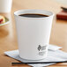 A white Dart ThermoGuard paper hot cup filled with coffee on a table with a napkin.