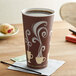 A brown and white Dart paper hot cup with white swirls on it full of coffee on a table with a straw on a napkin.