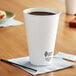 A white Dart ThermoGuard paper hot cup on a table with a lid on it.